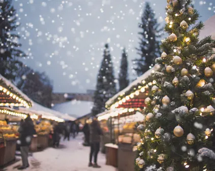 Bild som illustrerar Firefly Julmarknad Med Marknadsstånd, Utomhus, Granar Med Ljulgransljus Och Stjärna I Toppen, Snöfli