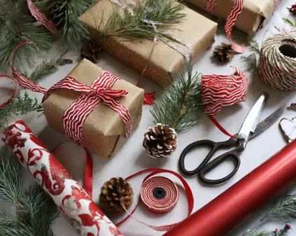 Bild som illustrerar Firefly Ett Bord Fyllt Med Julklappspapper, Sax, Presentsnören, Granris, Grankottar. Fotograferat Ov (1)